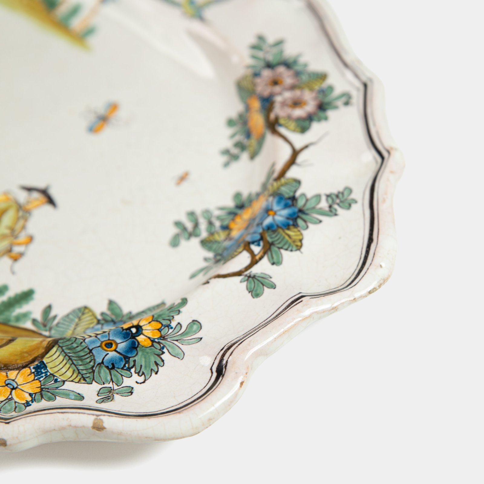 Oval faience plate, France, ca. 1760–1790, attributed to Rouen; tin-glazed earthenware with hand-painted chinoiserie scene in enamel pigments (cobalt, manganese, copper, antimony); figures in stylized garden within manganese-lined scalloped rim; ivory glaze with fine, stable craquelure
