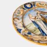 Hand-painted Italian maiolica plate, Deruta or Urbino, late 17th to early 18th century. Depicts Mercury with winged sandals beside a female figure, likely an allegory of Peace, Concord, or Wisdom. Rich Baroque border with cherubs, musical instruments, and cartouches. Tin-glazed earthenware with visible craquelure and minor rim losses.