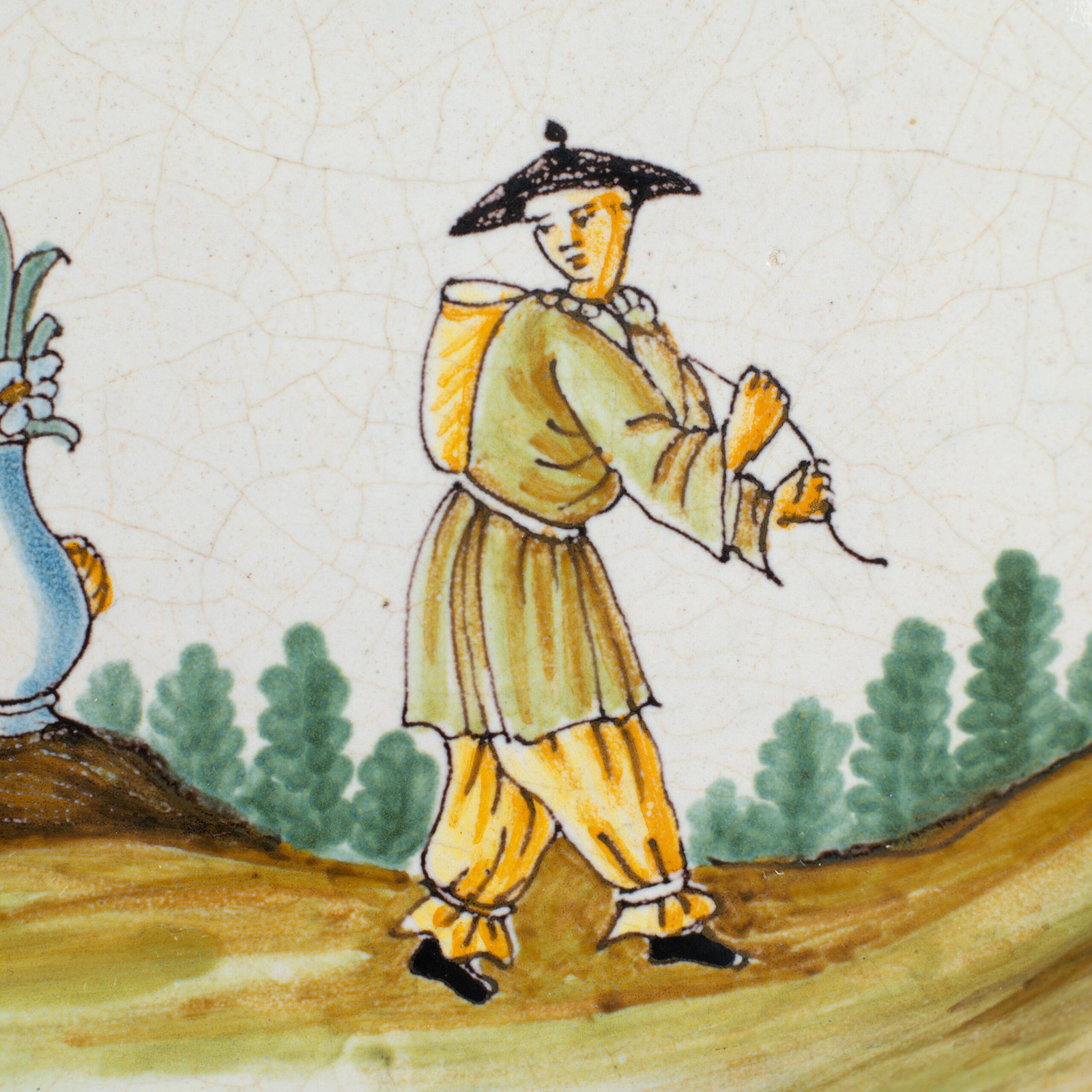Oval faience plate, France, ca. 1760–1790, attributed to Rouen; tin-glazed earthenware with hand-painted chinoiserie scene in enamel pigments (cobalt, manganese, copper, antimony); figures in stylized garden within manganese-lined scalloped rim; ivory glaze with fine, stable craquelure