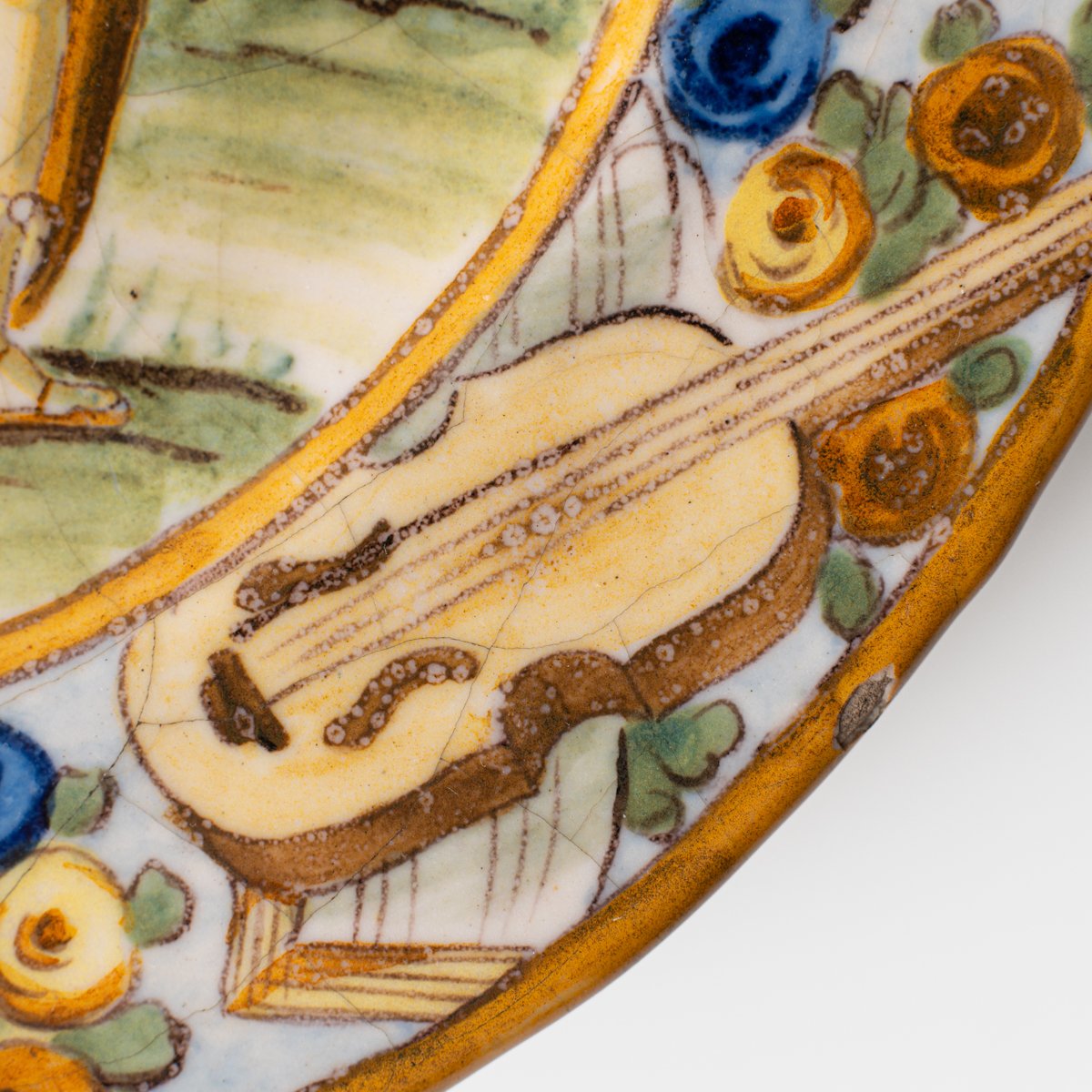 Hand-painted Italian maiolica plate, Deruta or Urbino, late 17th to early 18th century. Depicts Mercury with winged sandals beside a female figure, likely an allegory of Peace, Concord, or Wisdom. Rich Baroque border with cherubs, musical instruments, and cartouches. Tin-glazed earthenware with visible craquelure and minor rim losses.