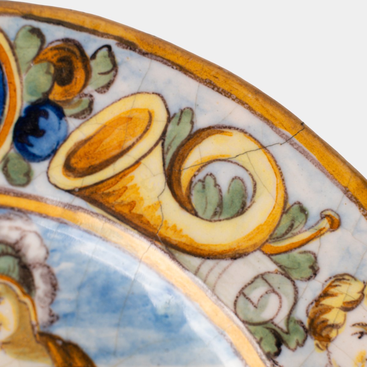 Hand-painted Italian maiolica plate, Deruta or Urbino, late 17th to early 18th century. Depicts Mercury with winged sandals beside a female figure, likely an allegory of Peace, Concord, or Wisdom. Rich Baroque border with cherubs, musical instruments, and cartouches. Tin-glazed earthenware with visible craquelure and minor rim losses.