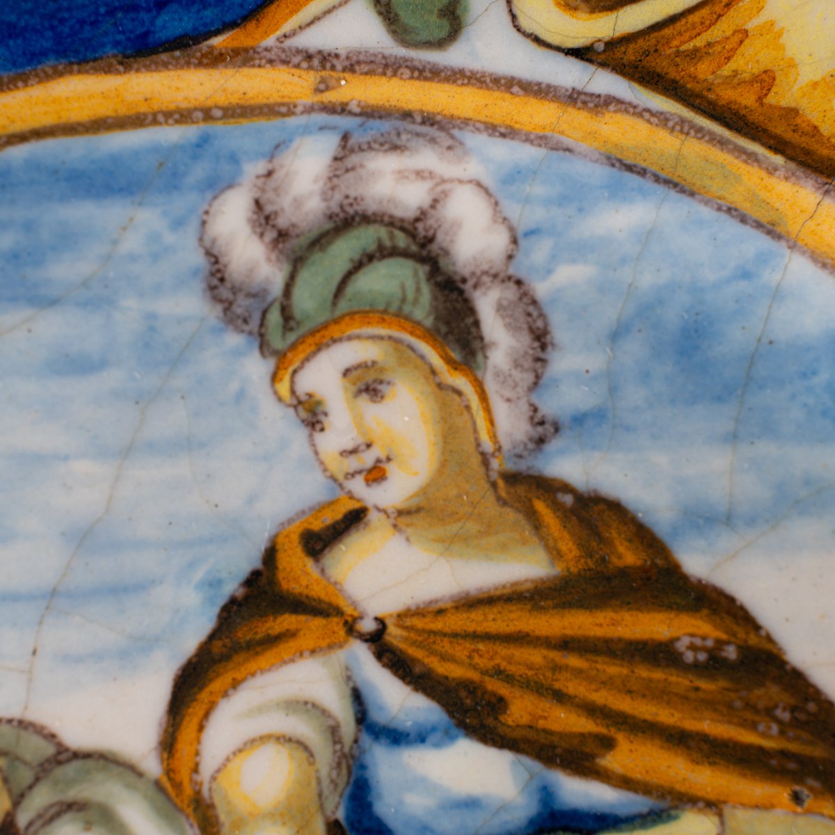 Hand-painted Italian maiolica plate, Deruta or Urbino, late 17th to early 18th century. Depicts Mercury with winged sandals beside a female figure, likely an allegory of Peace, Concord, or Wisdom. Rich Baroque border with cherubs, musical instruments, and cartouches. Tin-glazed earthenware with visible craquelure and minor rim losses.