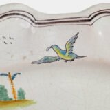 Oval faience plate, France, ca. 1760–1790, attributed to Rouen; tin-glazed earthenware with hand-painted chinoiserie scene in enamel pigments (cobalt, manganese, copper, antimony); figures in stylized garden within manganese-lined scalloped rim; ivory glaze with fine, stable craquelure