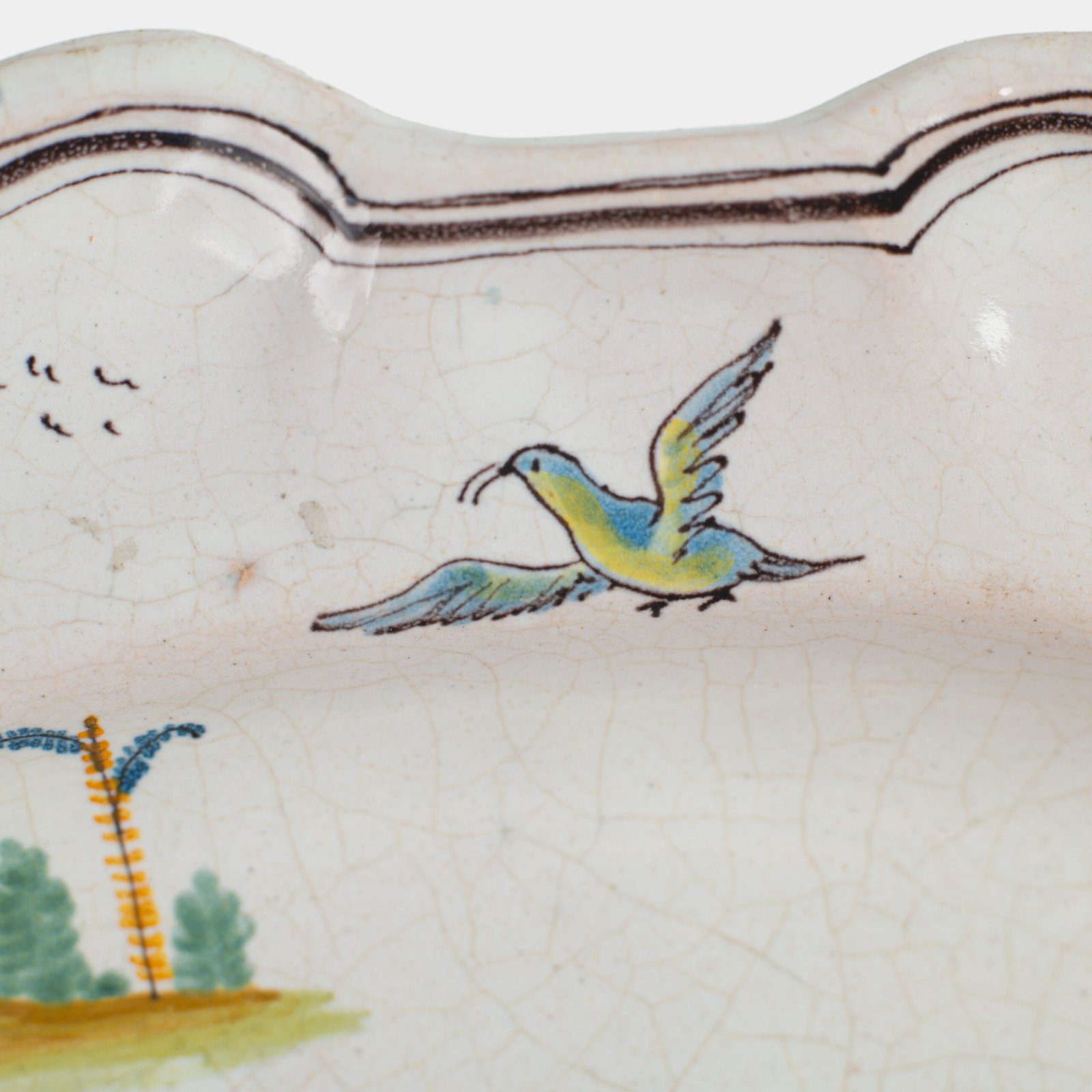 Oval faience plate, France, ca. 1760–1790, attributed to Rouen; tin-glazed earthenware with hand-painted chinoiserie scene in enamel pigments (cobalt, manganese, copper, antimony); figures in stylized garden within manganese-lined scalloped rim; ivory glaze with fine, stable craquelure