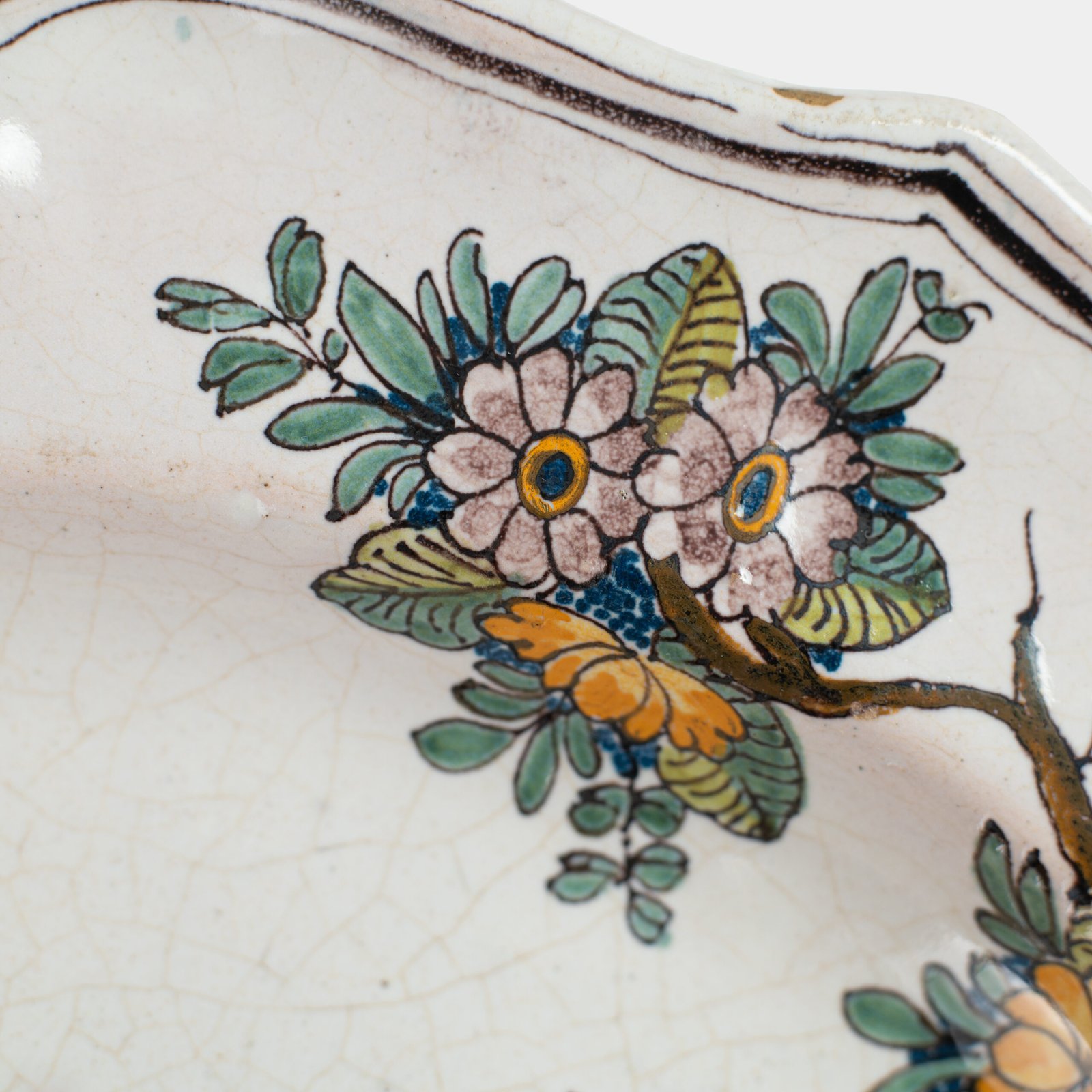 Oval faience plate, France, ca. 1760–1790, attributed to Rouen; tin-glazed earthenware with hand-painted chinoiserie scene in enamel pigments (cobalt, manganese, copper, antimony); figures in stylized garden within manganese-lined scalloped rim; ivory glaze with fine, stable craquelure