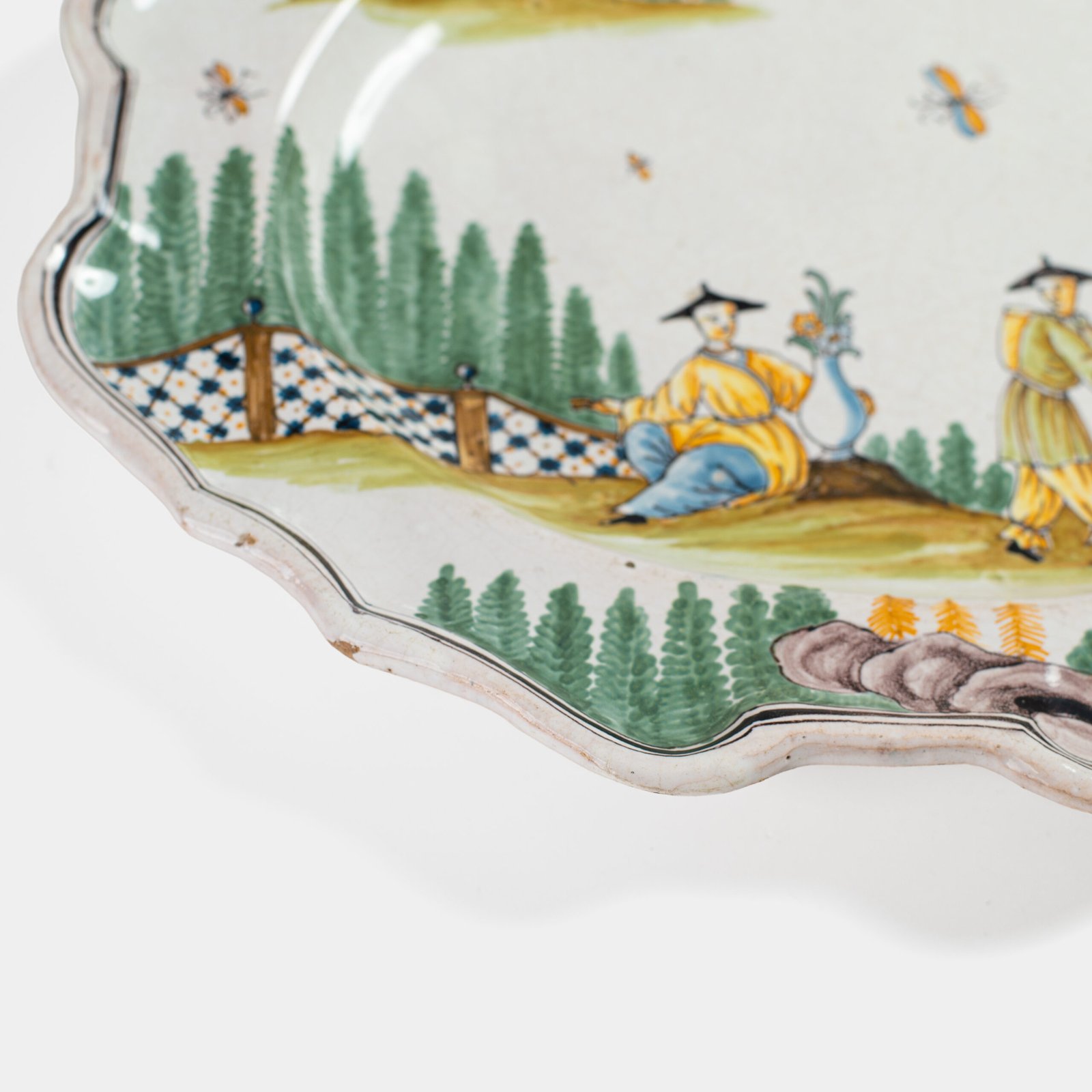 Oval faience plate, France, ca. 1760–1790, attributed to Rouen; tin-glazed earthenware with hand-painted chinoiserie scene in enamel pigments (cobalt, manganese, copper, antimony); figures in stylized garden within manganese-lined scalloped rim; ivory glaze with fine, stable craquelure