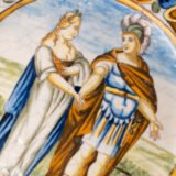 Hand-painted Italian maiolica plate, Deruta or Urbino, late 17th to early 18th century. Depicts Mercury with winged sandals beside a female figure, likely an allegory of Peace, Concord, or Wisdom. Rich Baroque border with cherubs, musical instruments, and cartouches. Tin-glazed earthenware with visible craquelure and minor rim losses.