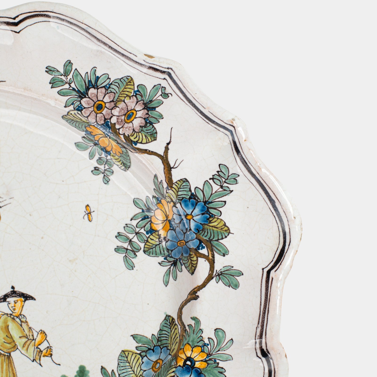 Oval faience plate, France, ca. 1760–1790, attributed to Rouen; tin-glazed earthenware with hand-painted chinoiserie scene in enamel pigments (cobalt, manganese, copper, antimony); figures in stylized garden within manganese-lined scalloped rim; ivory glaze with fine, stable craquelure