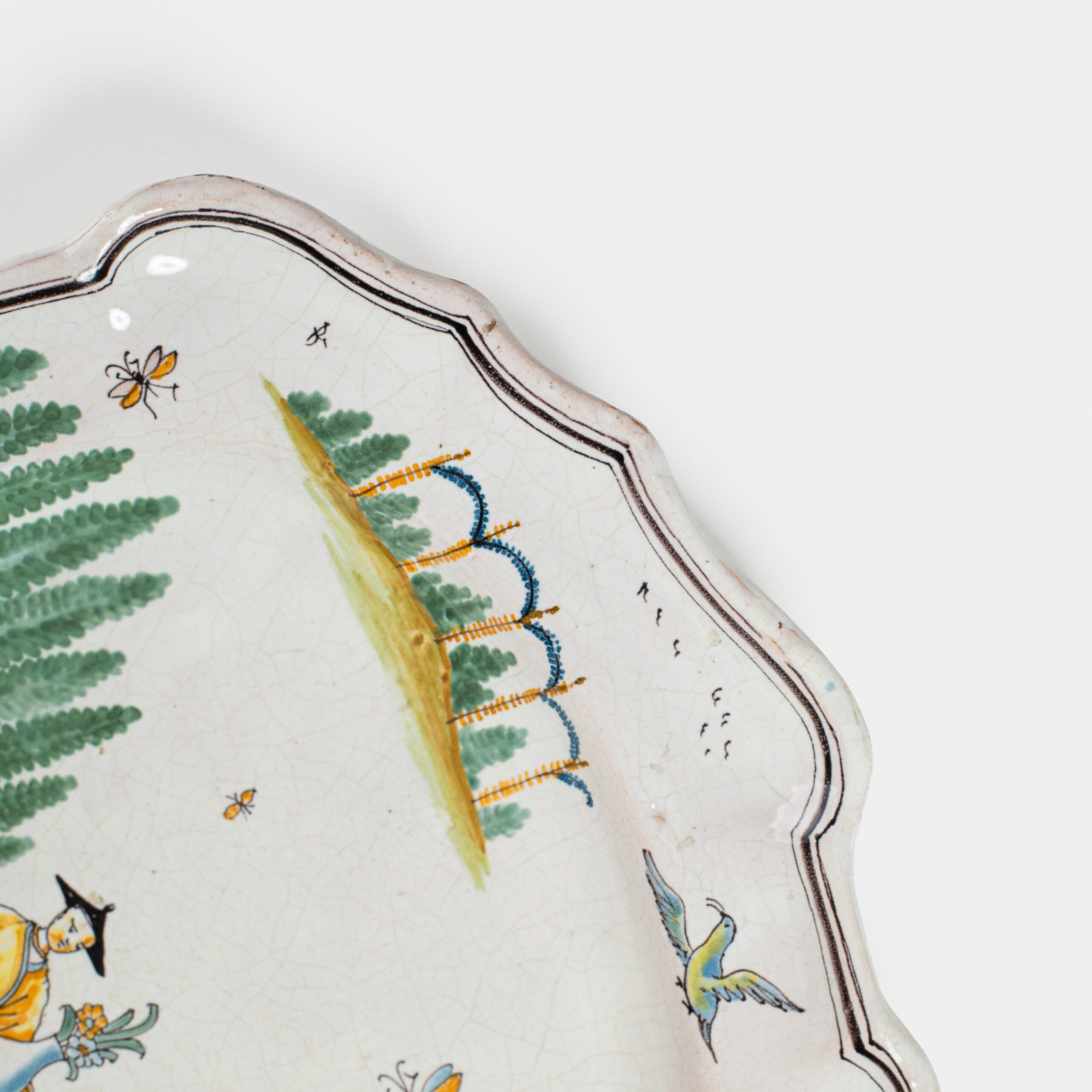 Oval faience plate, France, ca. 1760–1790, attributed to Rouen; tin-glazed earthenware with hand-painted chinoiserie scene in enamel pigments (cobalt, manganese, copper, antimony); figures in stylized garden within manganese-lined scalloped rim; ivory glaze with fine, stable craquelure