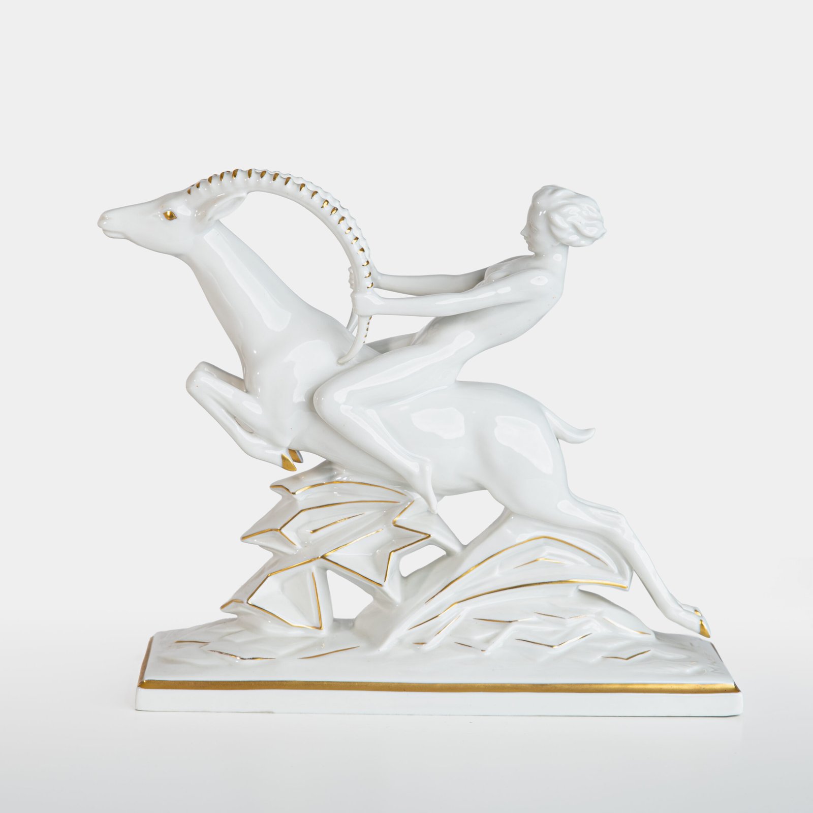Glazed white porcelain sculpture signed by Max Hermann Fritz and produced by Hutschenreuther Selb between 1925 and 1935. Depicts a nude female figure riding a leaping ibex, with hand-applied gilding on the horns, eyes, hooves, and base. German Art Deco style.