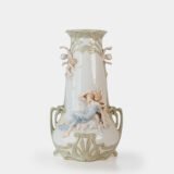 Art Nouveau porcelain vase by Karl Ens, circa 1900, featuring a sculptural composition in high relief with a maiden and cherub, hand-painted with floral details and highlighted with gilding. Marked “KVE” on the base.