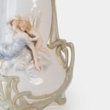 Art Nouveau porcelain vase by Karl Ens, circa 1900, featuring a sculptural composition in high relief with a maiden and cherub, hand-painted with floral details and highlighted with gilding. Marked “KVE” on the base.
