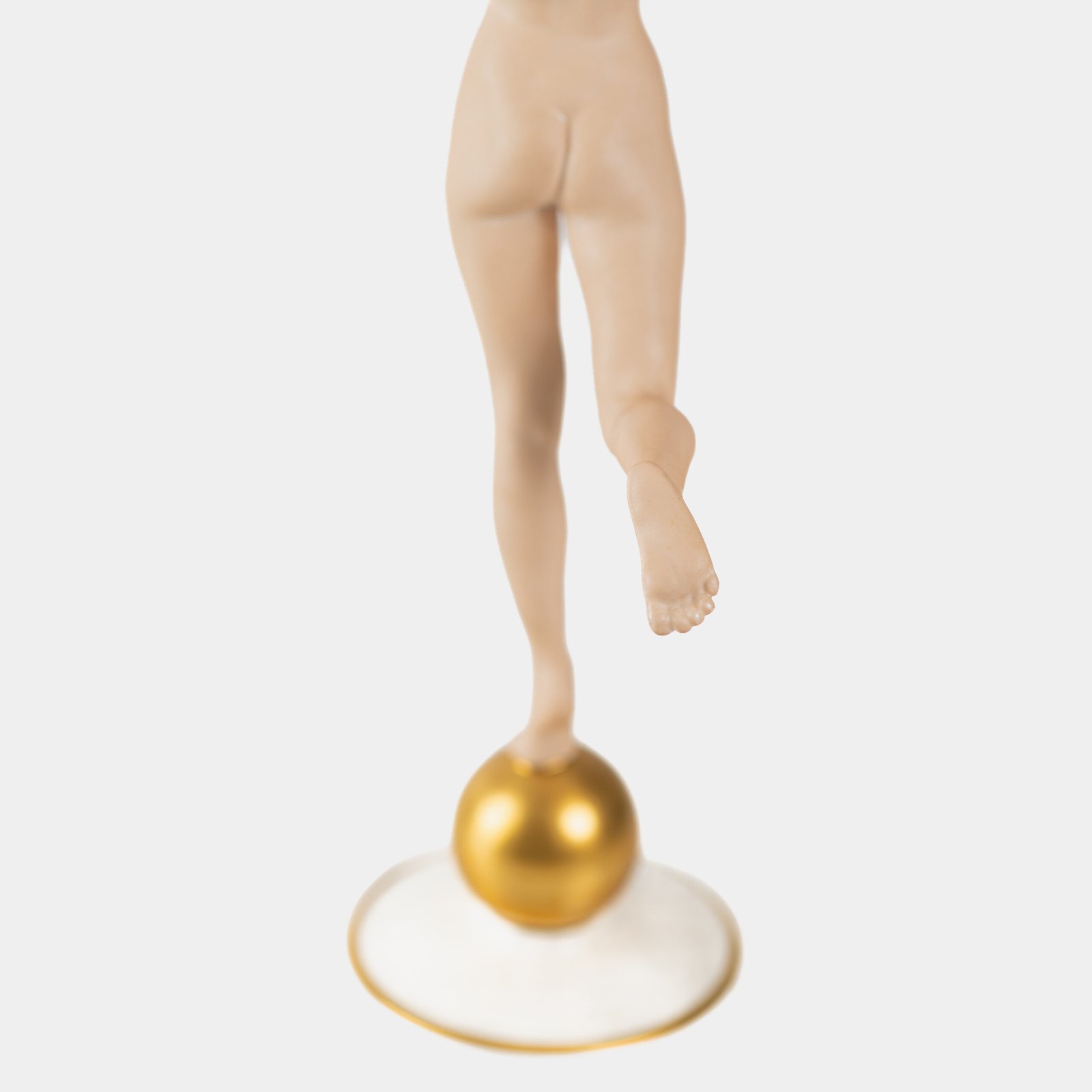 Karl Tutter porcelain figurine “Sonnenkind” – Art Deco sculpture by Hutschenreuther Germany, c.1935–1940 Art Deco porcelain figurine titled “Sonnenkind” (“Sun Child”), modeled by Karl Tutter for Hutschenreuther ca. 1935–1940. Depicts a nude young woman balancing on a golden sphere, arms extended in a dynamic pose. White porcelain with a matte pinkish flesh-tone finish, painted facial features, and satin brown hair. Gilded accents on the sphere and base. Rare signed version with circular base and gold trim.