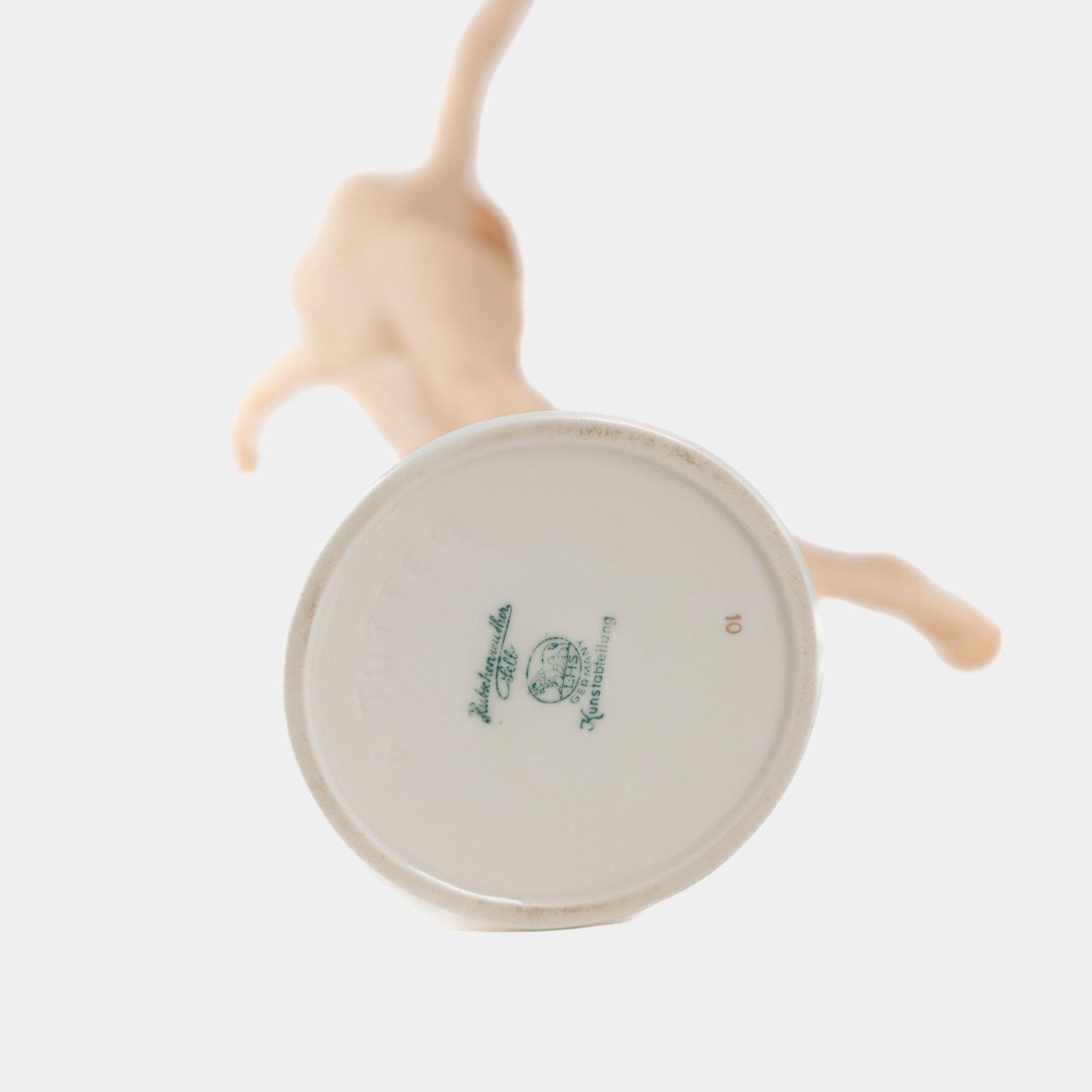 Karl Tutter porcelain figurine “Sonnenkind” – Art Deco sculpture by Hutschenreuther Germany, c.1935–1940 Art Deco porcelain figurine titled “Sonnenkind” (“Sun Child”), modeled by Karl Tutter for Hutschenreuther ca. 1935–1940. Depicts a nude young woman balancing on a golden sphere, arms extended in a dynamic pose. White porcelain with a matte pinkish flesh-tone finish, painted facial features, and satin brown hair. Gilded accents on the sphere and base. Rare signed version with circular base and gold trim.