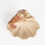 Royal Dux Art Nouveau porcelain centerpiece with a seated maiden and fawn beside a green shell-shaped bowl, hand-painted with gilt highlights, circa 1920–1930.