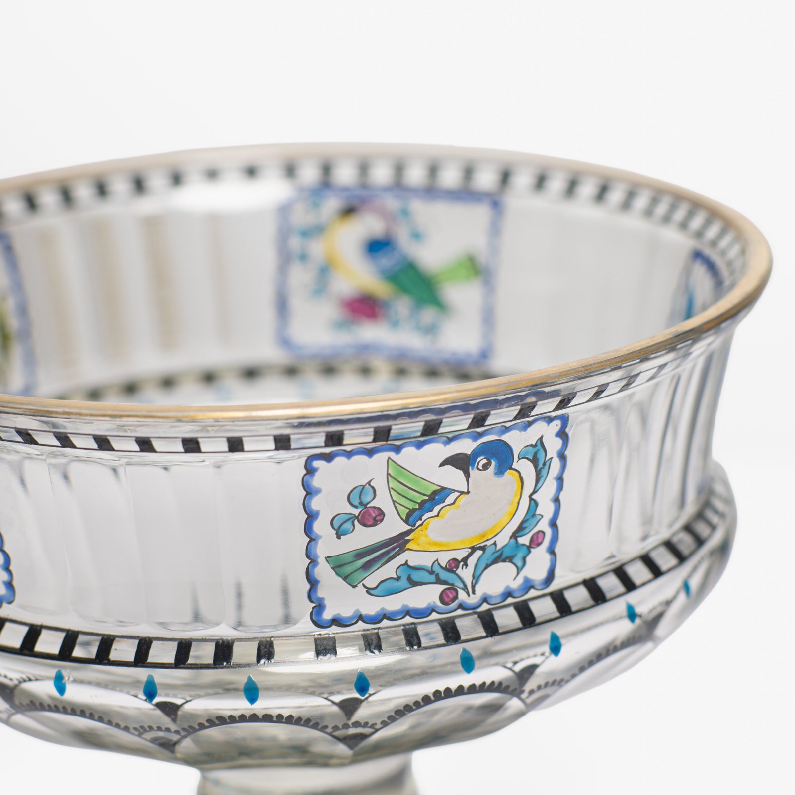 Bohemian Glass Compote, c. 1915, with hand-enamelled birds in scalloped blue panels, geometric glass cutting, gilt rim and a faceted foot decorated with black scrolls and blue leaves.